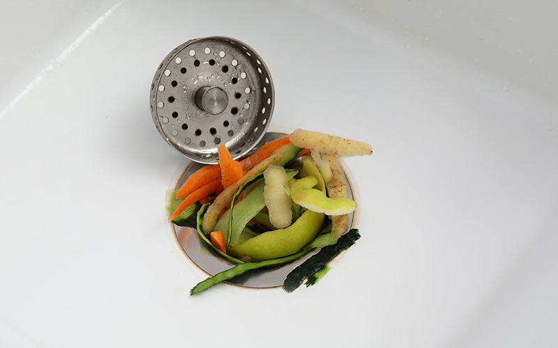 Kitchen sink strainer filled with food waste and vegetable peels.