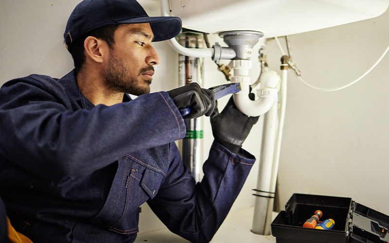 Professional plumber using a wrench to repair under-sink drainage.